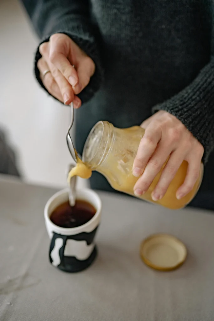 Adding a spoon of whipped honey in a coffee cup